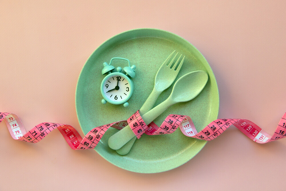 Creative Flat Lay Composition With Plate Alarm Clock Spoon Fork And Measuring Tape On Pink Background