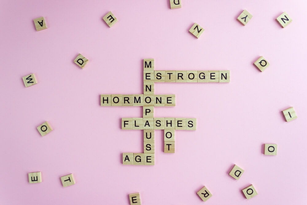 Word Menopause, Esrogen, Hormone, Age and Hot Flashes on wooden blocks on pink background.