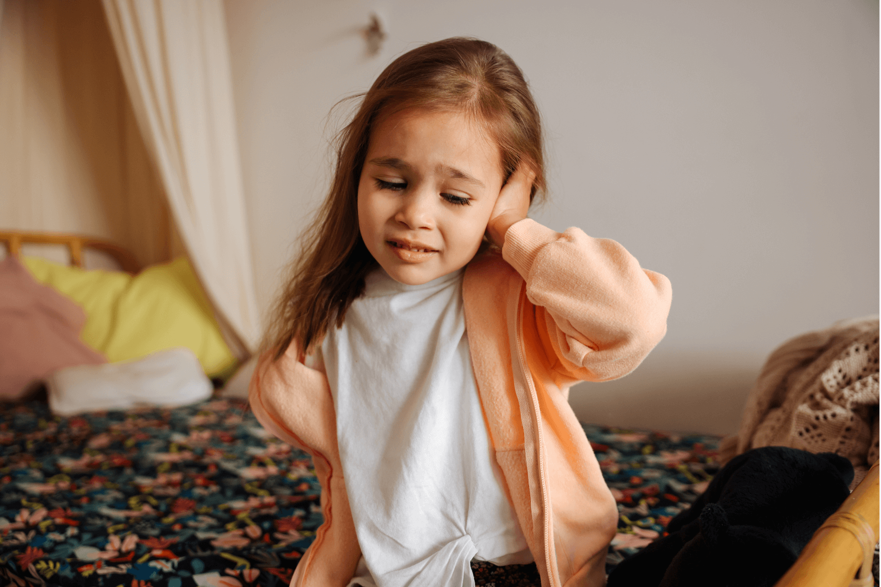 A little girl with ear pain and holding her hand on her ear.