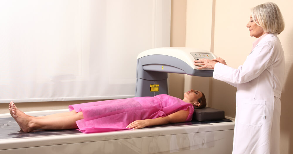 Female Doctor Examining Woman in 40s at Bone Densitometer Machine.