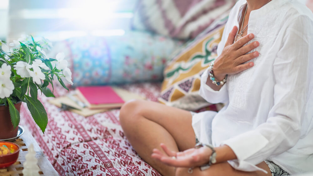 Woman Sitting in a Lotus Position With Right Hand on Heart Chakra and Left Palm Open in a Receiving Gesture.