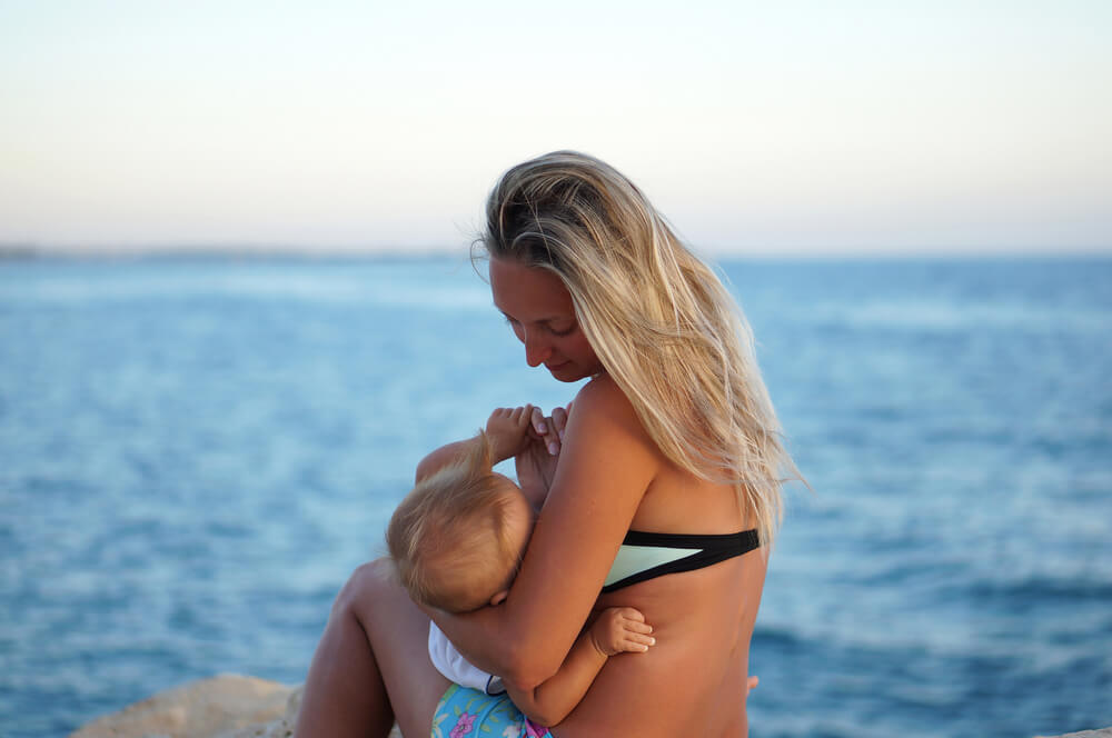 Mother Breastfeeding Baby on the Beach at Sunset Near the Sea