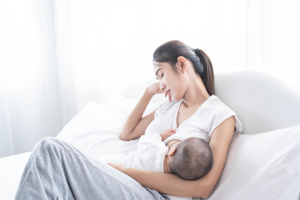 Tired Mother Breastfeeding Her Newborn Baby Next to a Window