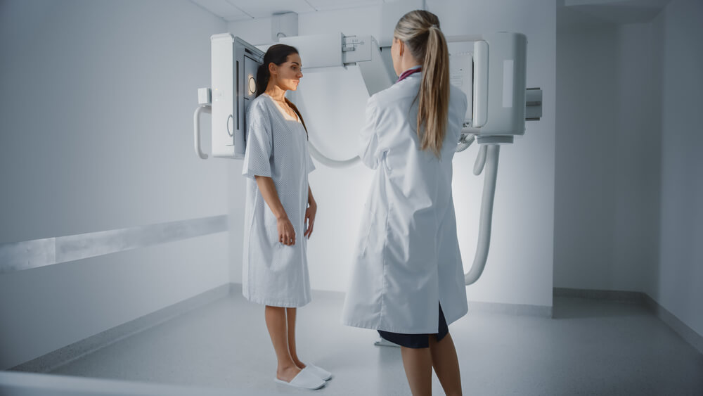 Woman in Medical Gown Standing Next to X-Ray Machine While Female Doctor Adjusts It