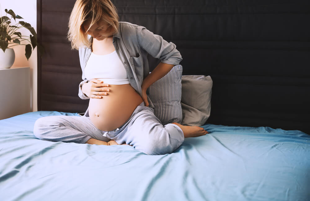 Beautiful Pregnant Woman Holds Hands on Her Belly and Lying in Bed at Home