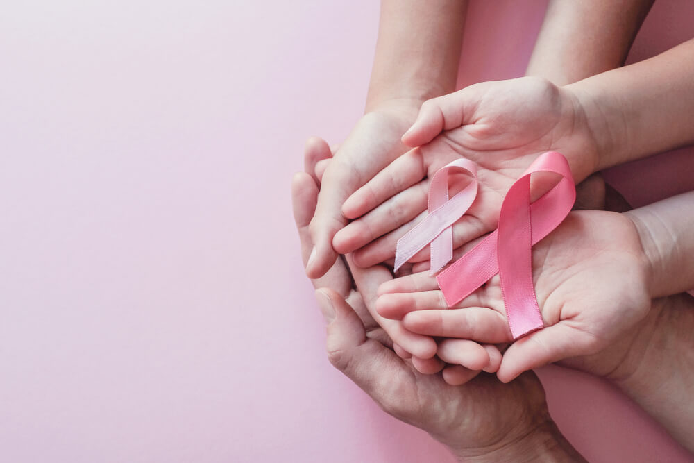 Hands Holding Pink Ribbons on Pink Background, Breast Cancer Awareness