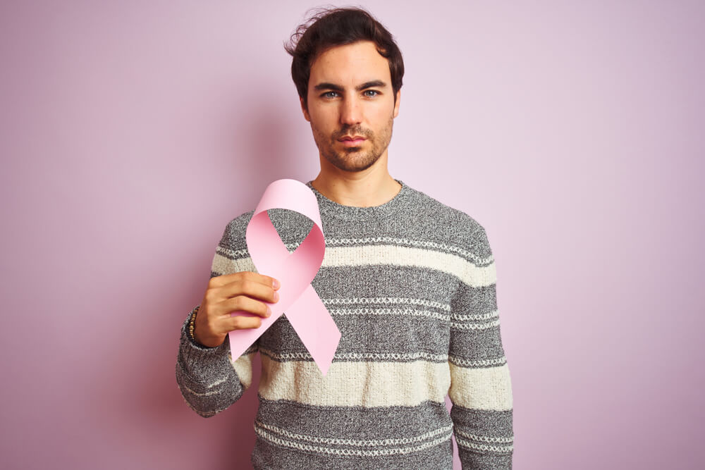 Young Handsome Man Holding Cancer Ribbon Standing Over Isolated Pink Background 