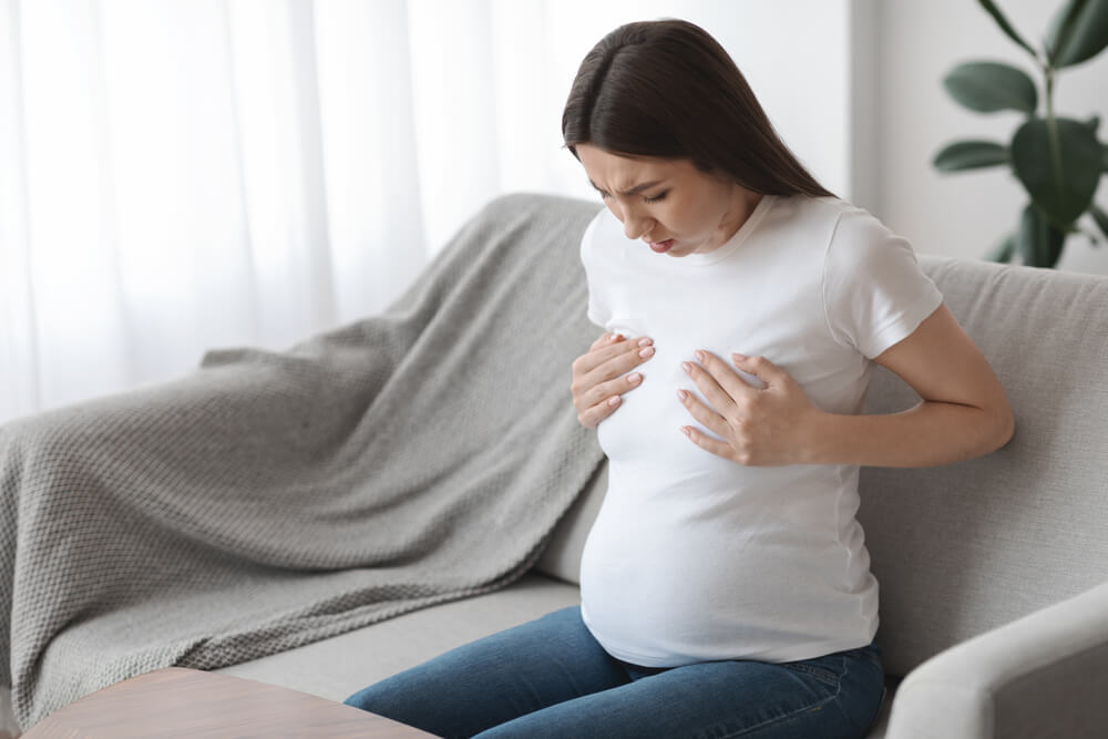 Concerned Pregnant Lady Touching Her Chest Area, Suffering Acute Pain, Massaging Herself While Sitting on Couch at Home