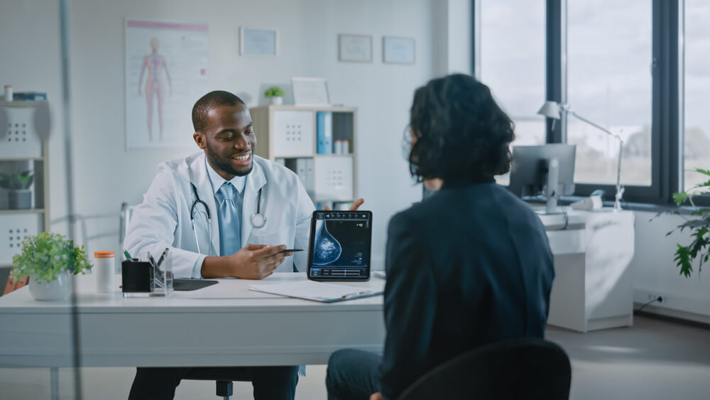 African American Medical Doctor Showing Mammography Test Results to a Patient on a Tablet Computer in a Health Clinic