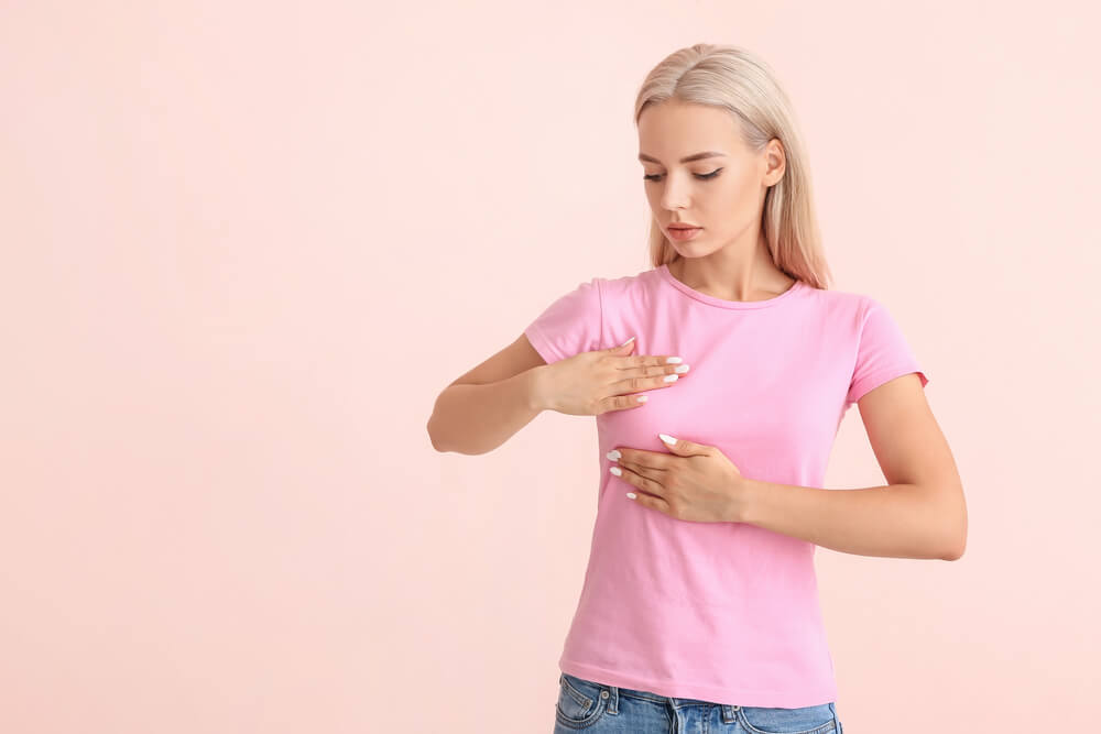 Young Woman Checking Her Breast on Color Background