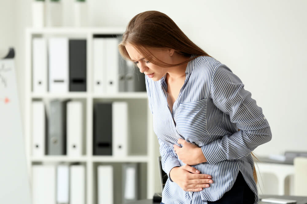 Young Woman Suffering From Abdominal Pain in Office