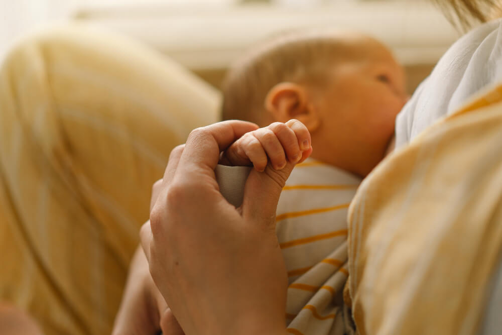 Newborn baby boy sucking milk from mothers breast.