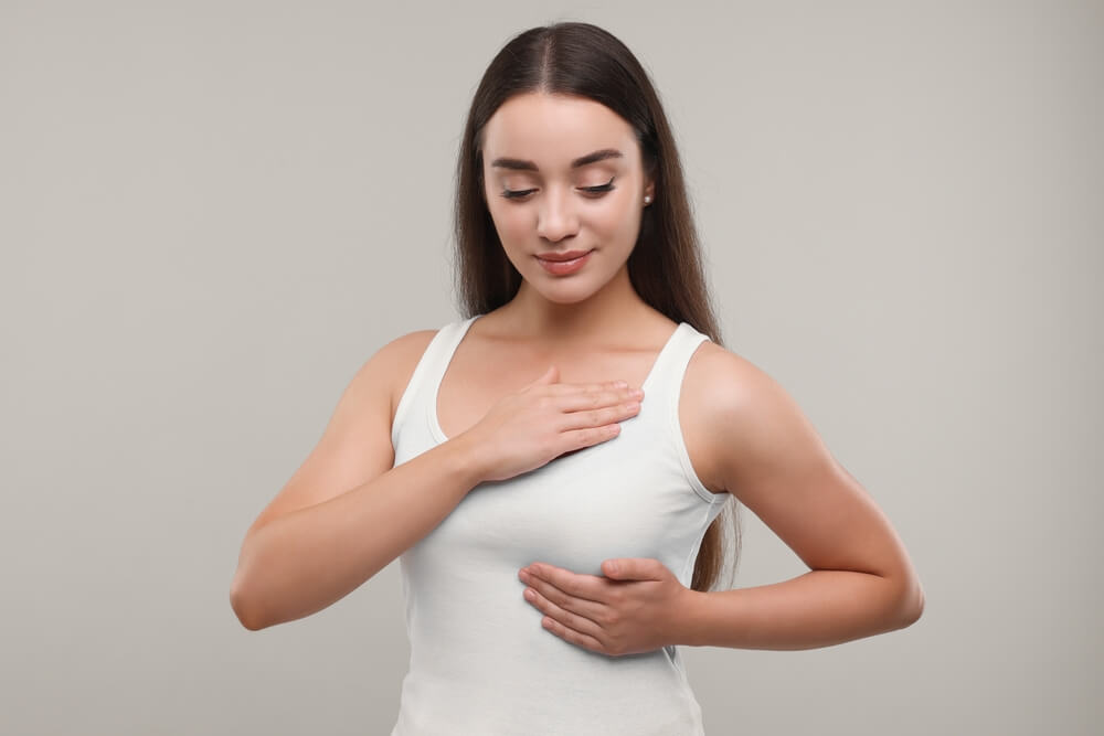 A young woman doing breast self-examination on light grey background