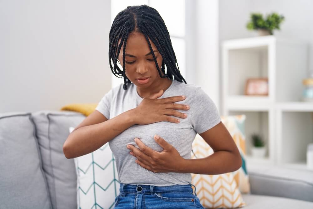 A woman examining breast sitting on sofa at home