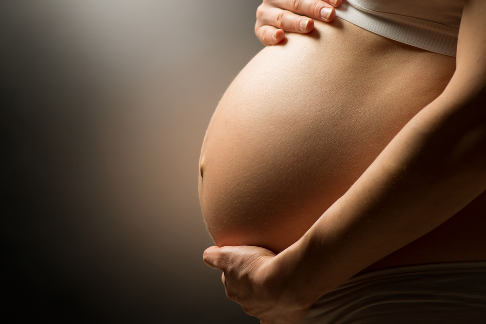 A Pregnant woman holding her belly in a dimly lit room