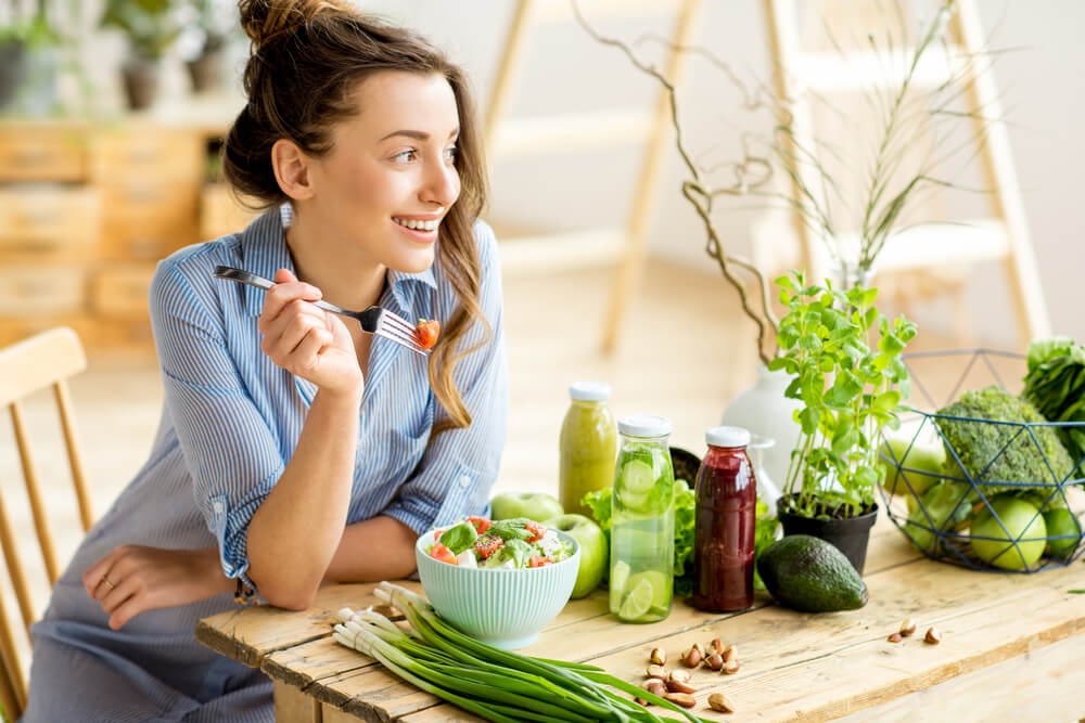 Young and Happy Woman Eating Healthy Salad Sitting at the Table