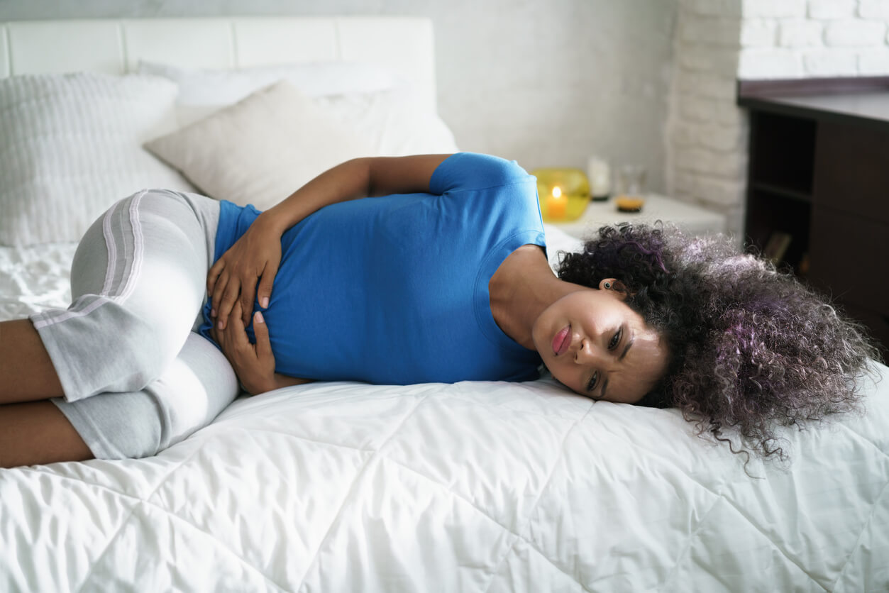 Sad Young Latina Woman With Menstrual Pain. Black Girl Having Cramps During Period and Lying on Bed at Home