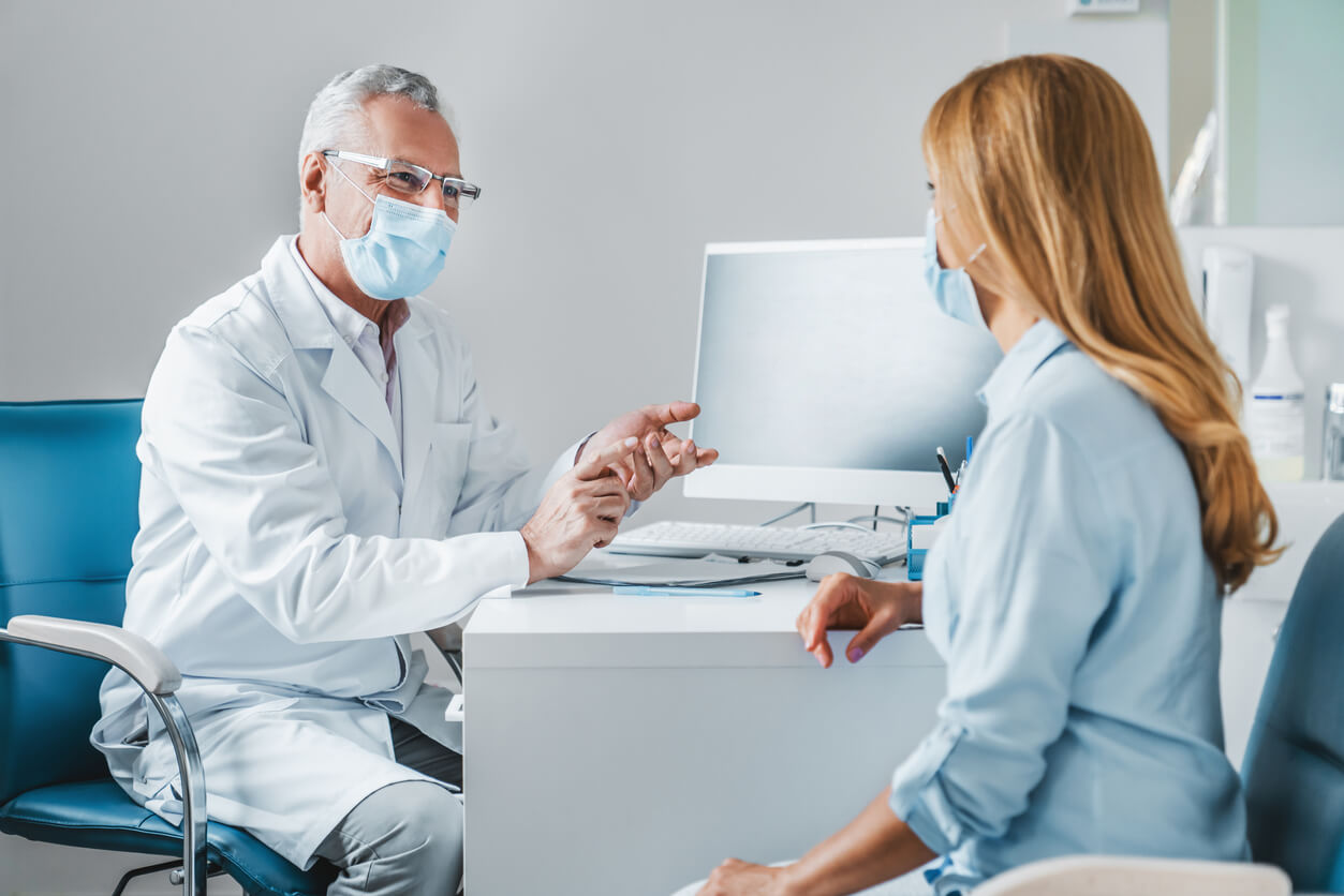 Senior Male Doctor Wear Protection Face Mask Talking With Patient in Clinic Office