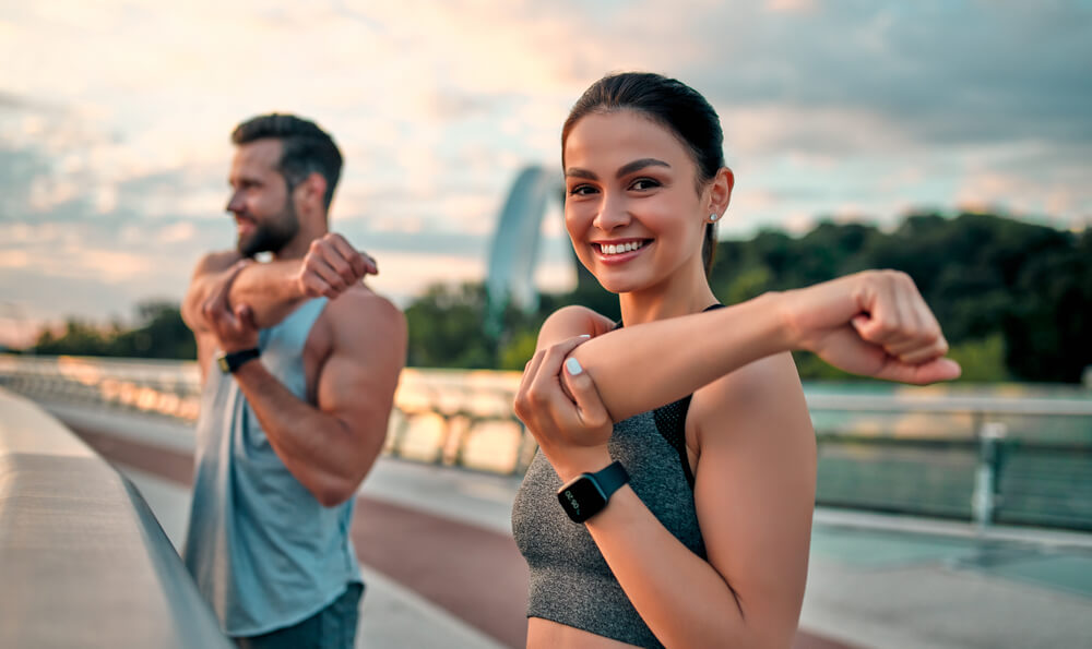 Couple Stretching Outdoors Before Morning Run. Handsome Bearded Man and Attractive Sporty Woman Running on the Street.