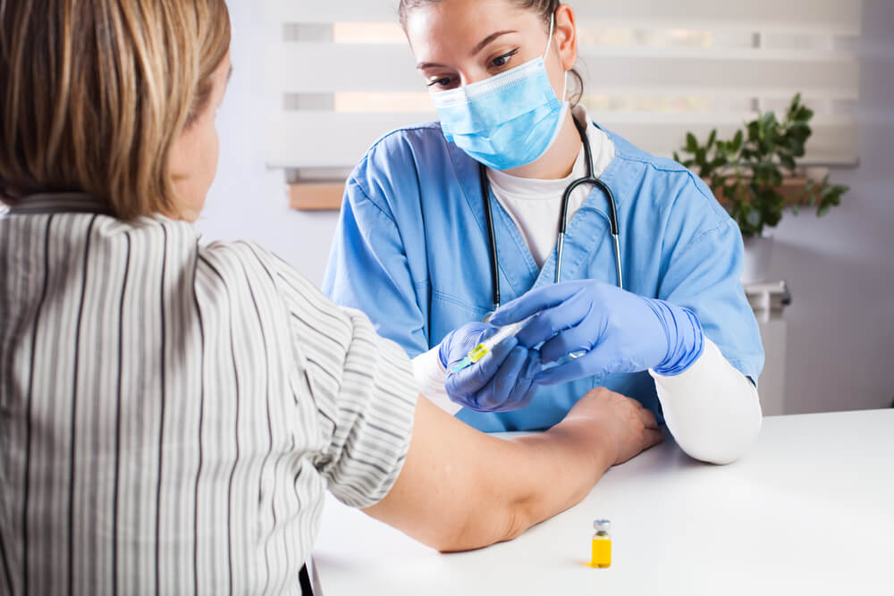 Young Female Doctor Vaccinating Elderly Patient in UK GP’s Office