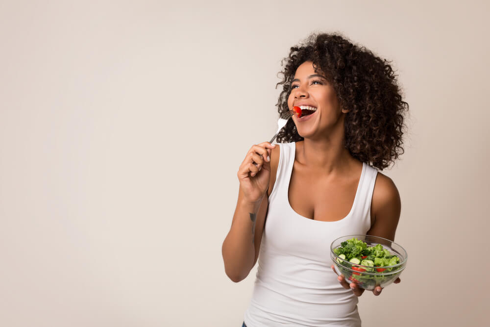 Excited African-American Lady Eating Healthy Salad Over Light Background
