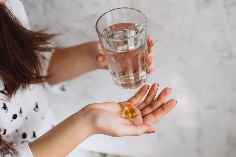 Girl’s Hands With Pills With Cod Liver Omega-3 Oil and a Glass of Fresh Water. 