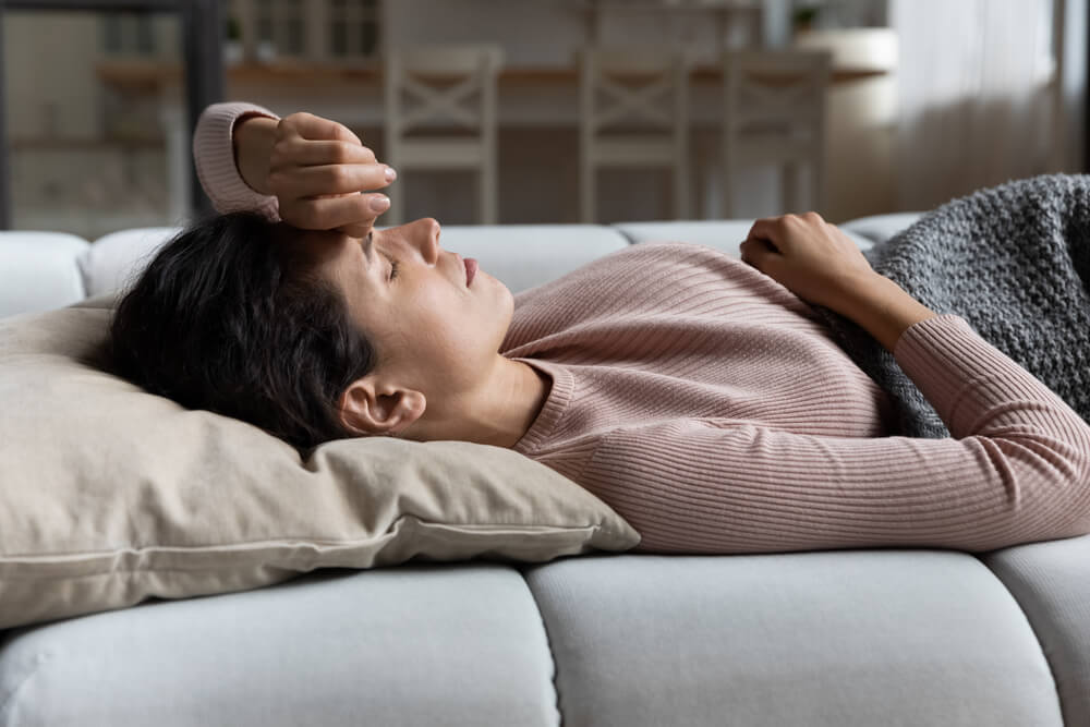 Weak Sick Millennial Hispanic Female Lying on Couch at Living Room Feel Dizzy Migraine Headache Suffer From Sleep Problem Disorder