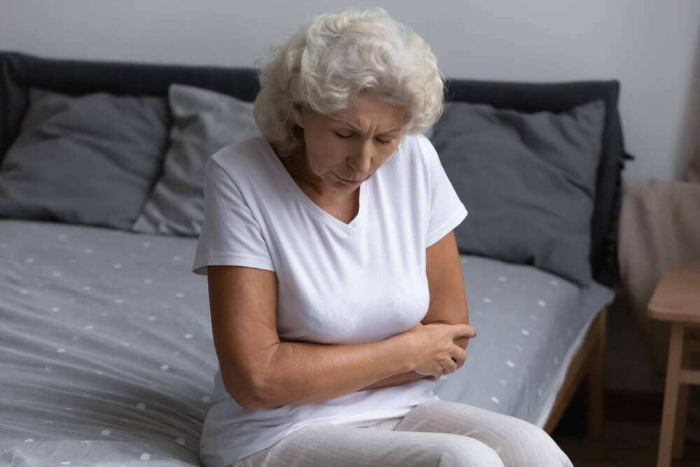 Unhappy Elderly Woman Sitting on Bed, Feeling Strong Belly Ache