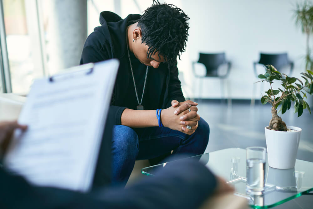 Sad African American Teenager Looking Down While Having a Therapy Session With His Psychiatrist.