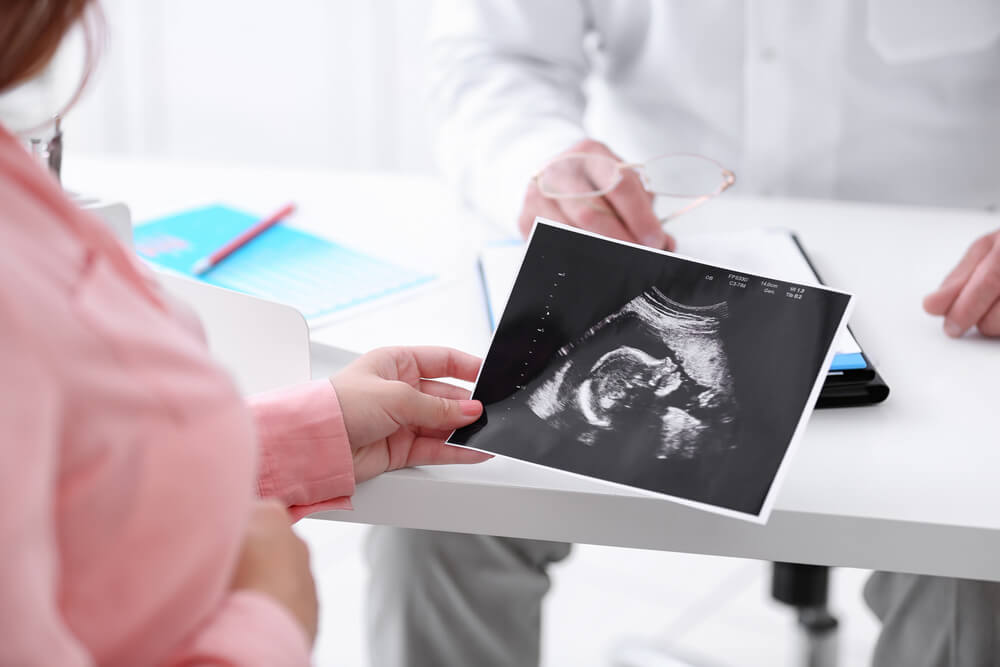 Young Pregnant Woman Visiting Doctor and Looking at Ultrasound Photo