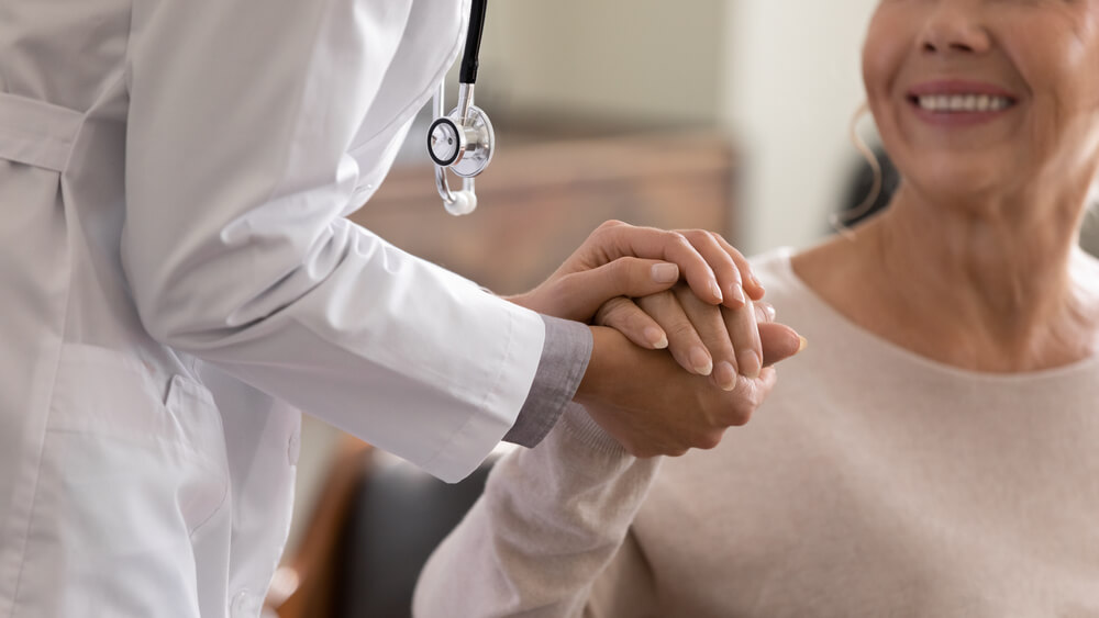Physician Leaning Forward to Smiling Elderly Lady Patient Holding Her Hand 