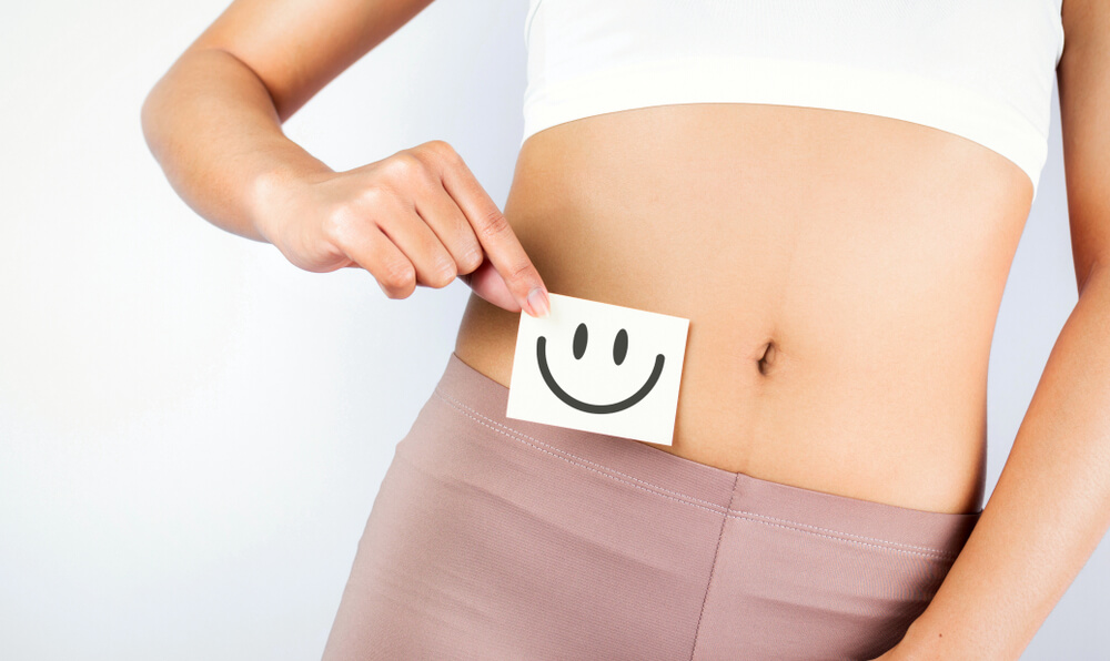 Healthy Woman Holding White Card With Happy Smiley Face in Hands Over Stomach 