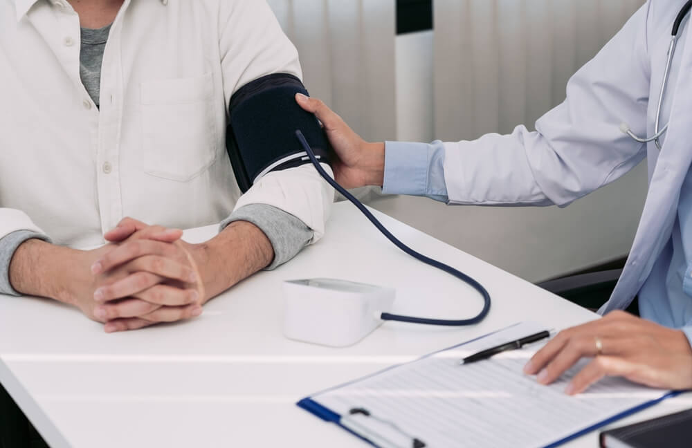 Asian Doctor Is Using A Patients Blood Pressure Monitor At The Time Of His Annual Check-up And Explains His Blood Pressure