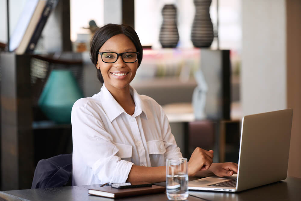 Beautiful Young Black Woman Smiling at Camera While Seated Behind Her Personal Computer