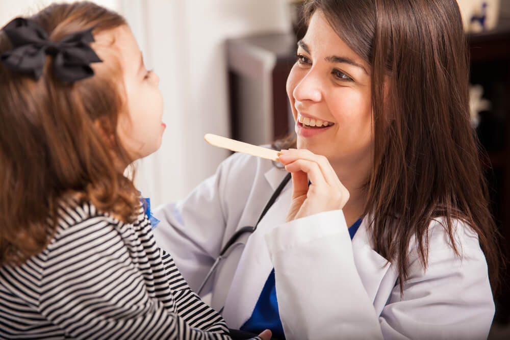 Portrait of a Beautiful Young Pediatrician Examining a Little Girl’s Mouth in a Clinic
