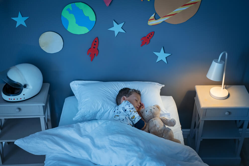 High Angle View of Little Boy Dreaming Of Becoming an Astronaut While Sleeping With Teddy Bear in Space Decorated Room