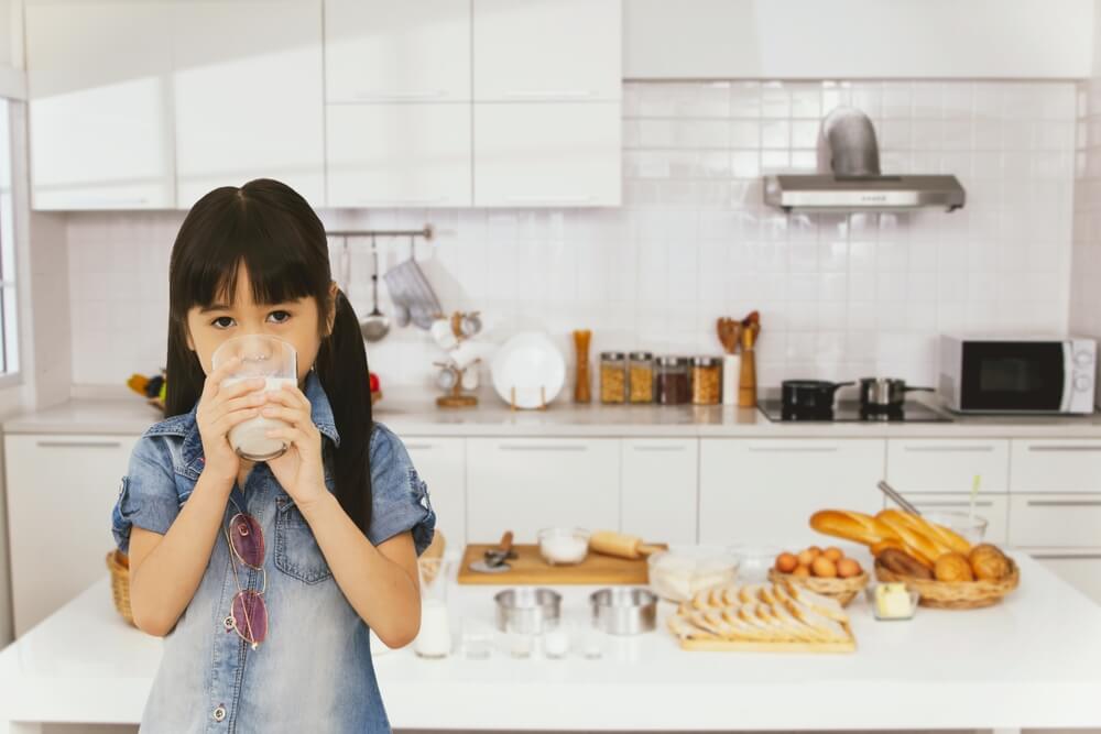 Cute Asian Woman Holding Glass Of Fresh Milk Standing Drinking Milk In Kitchen At Home