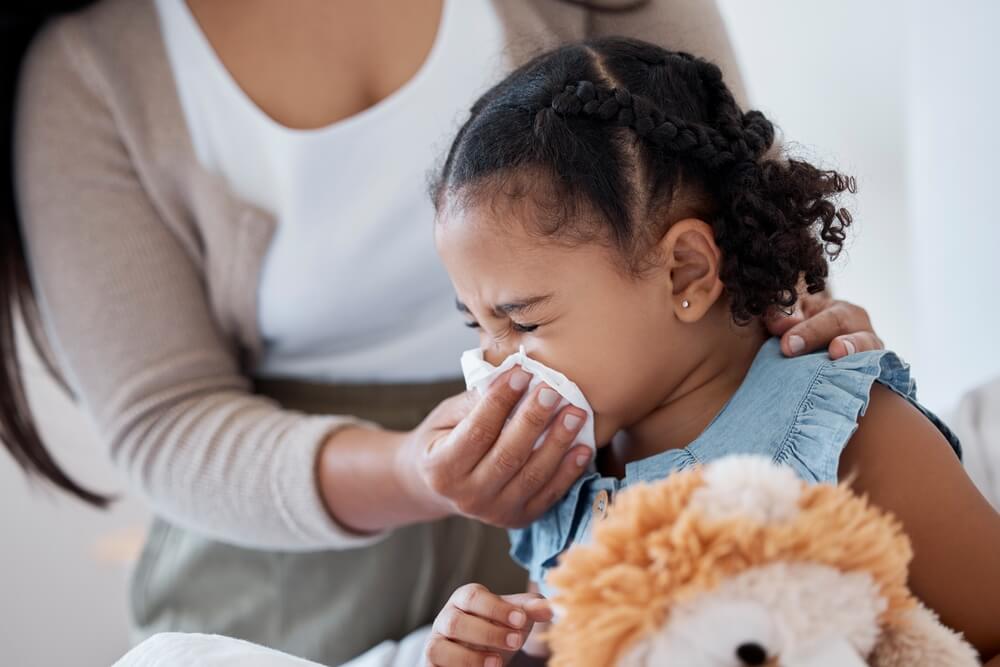 Mother Clean Sick Child Nose With Tissue Playing With Toy or Teddy Bear in Bedroom at Family Home