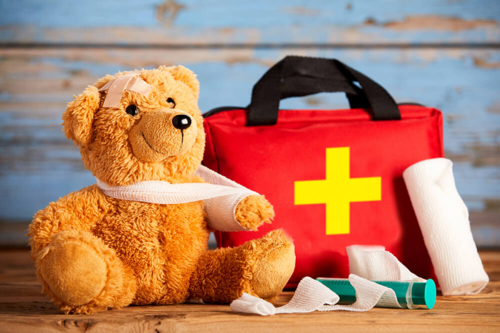 Paediatric Healthcare Concept With a Little Teddy Bear With Its Arm in a Sling Alongside a First Aid Kit and Bandages on Rustic Wood