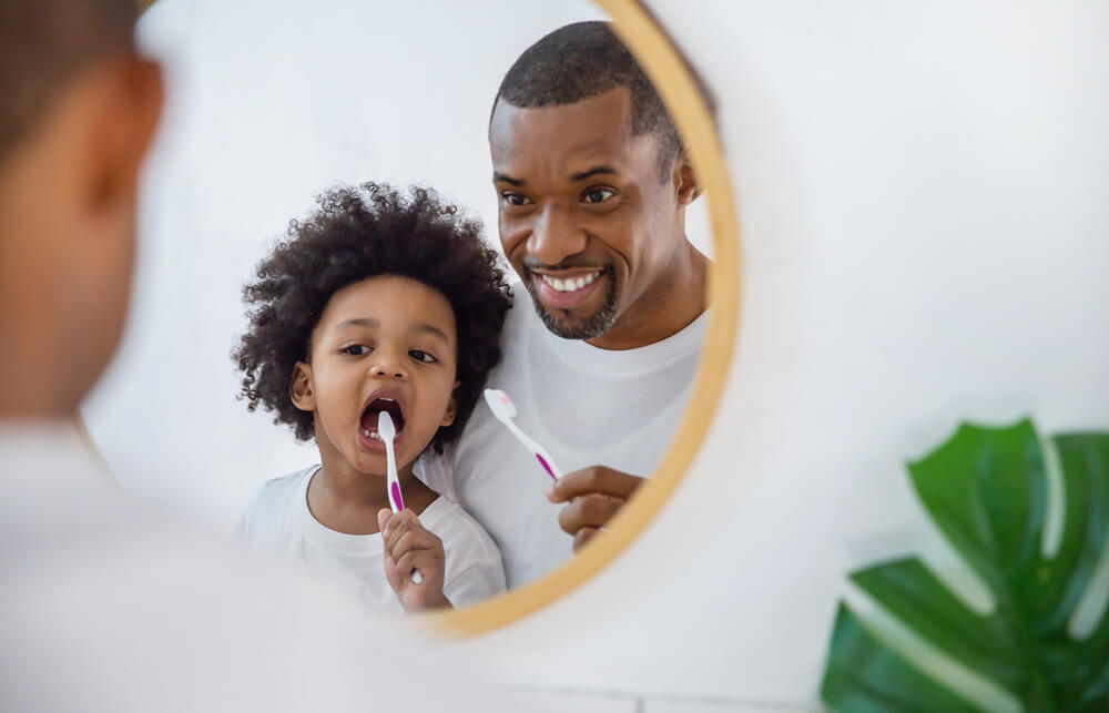 Portrait Of Happy Family Black African American Father And Son Child Boy Brushing Teeth In The Bathroom
