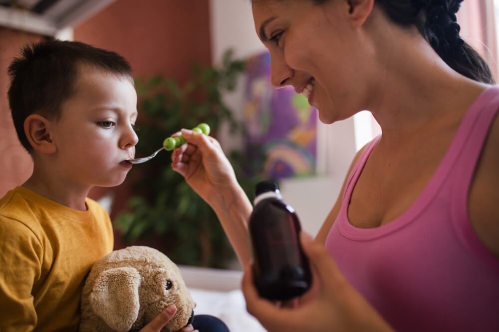 Young Mother Giving Medicines Coughing Syrup From Spoon To Her Sick Little Son