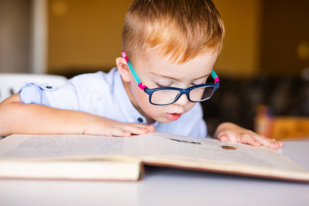 Boy With Down Syndrome With Big Glasses Reading Book