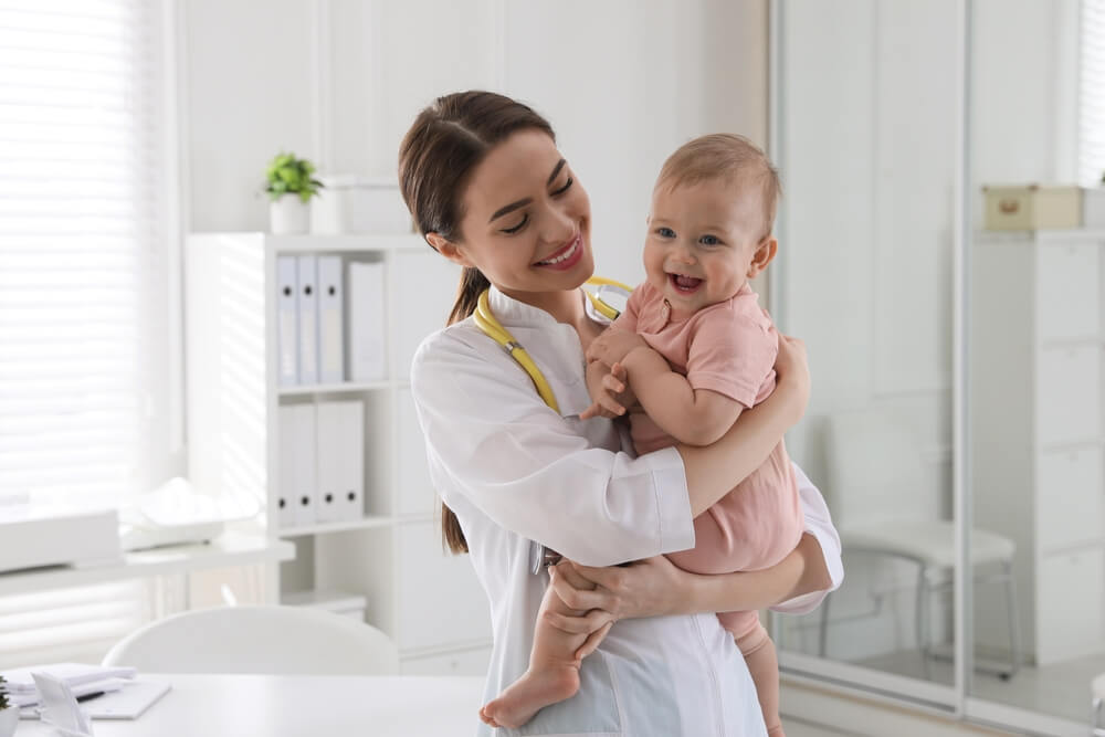 A young pediatrician holding a baby in her office.