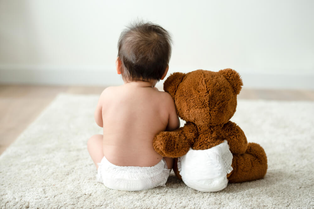 A baby with a teddy bear wearing diapers.