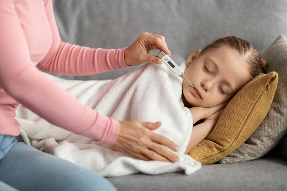 The mother is measuring the temperature of her ill daughter at home with an oral thermometer.