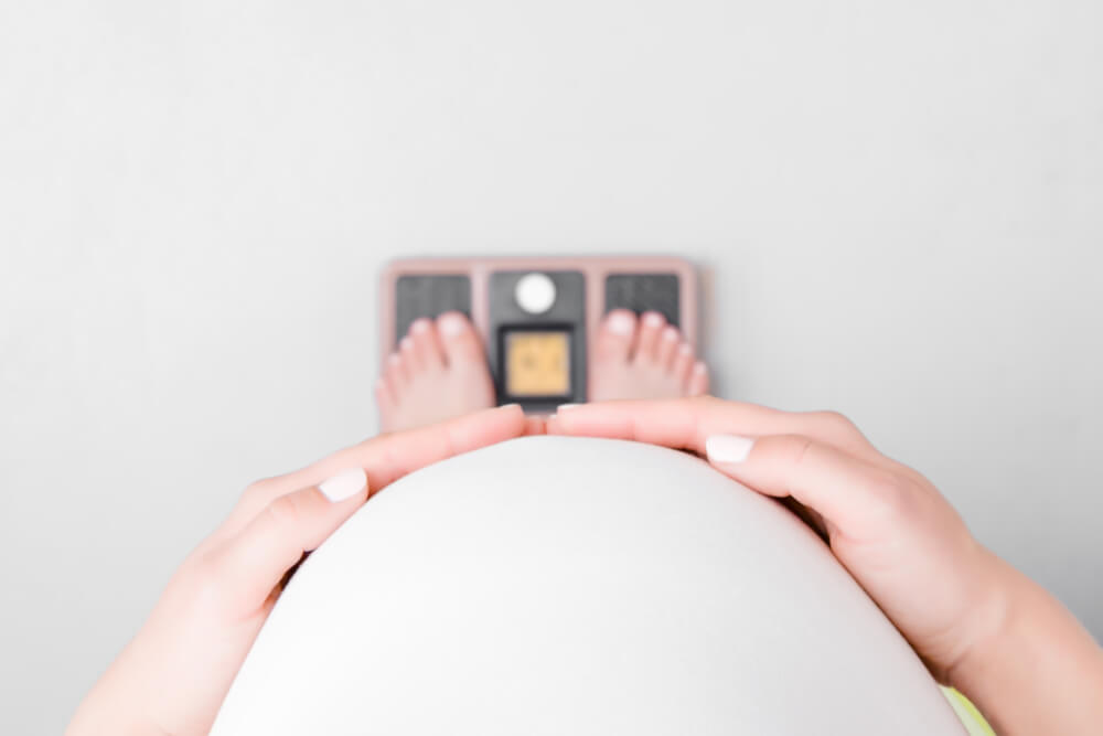 Pregnant Woman With Barefoot Standing on Weight Scales. Hands Touching Big Belly