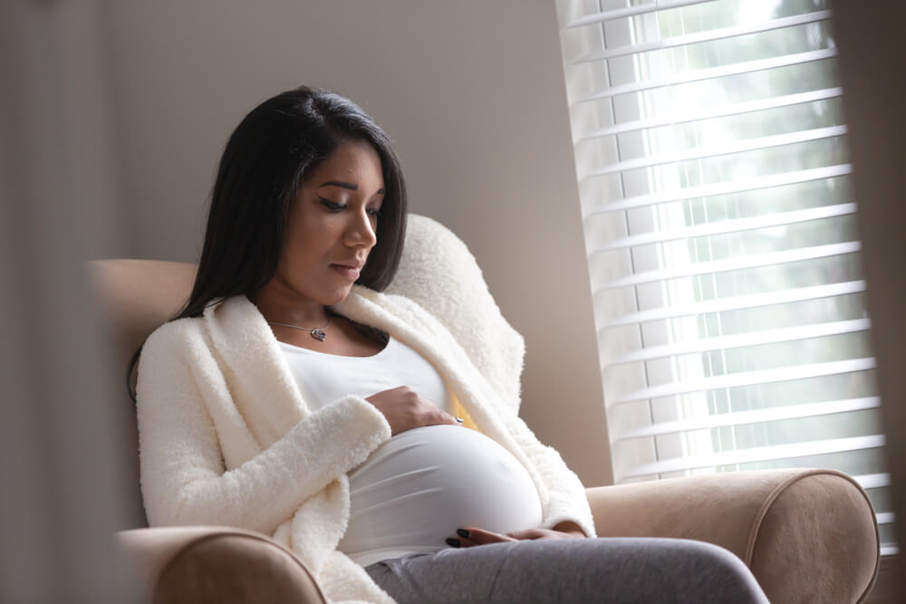 A Pregnant Woman Holding Her Belly in a Chair in Deep Thought