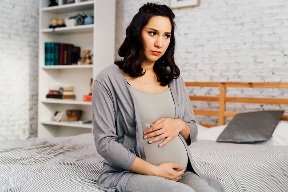 Concerned and Anxious Woman in Pregnancy Overthinking Sits on Bed at Home