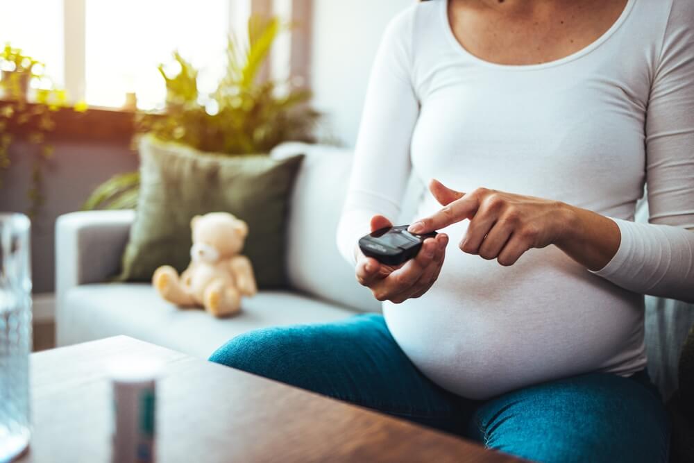 Pregnancy, Health and Glycemia Concept - Pregnant Beautiful Woman Checking Blood Sugar Level With Glucometer and Lancing Device at Home