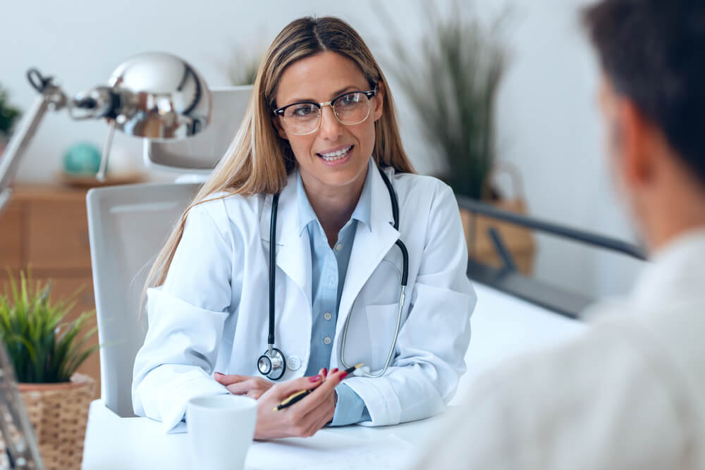 Shot of Beautiful Mature Female Doctor Talking While Explaining Medical Treatment While Prescribing Medication to Patient in the Consultation.